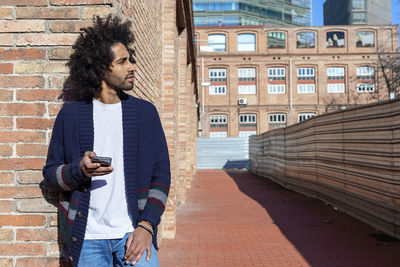 Young man using mobile phone standing against buildings