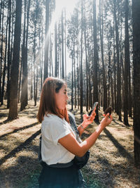 Side view of woman using mobile phone while holding pine cone in forest