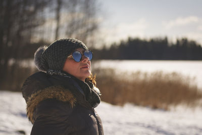 Side view of woman in warm clothing standing on snow covered field