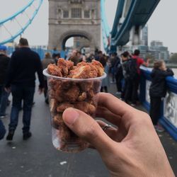 Close-up of cropped hand holding fried chicken in plastic container at tower bridge