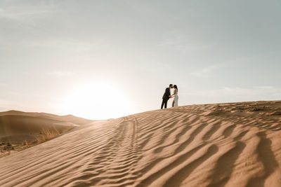 Man on sand dune in desert against sky