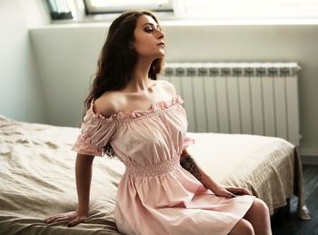 Beautiful young woman looking away while sitting on bed at home