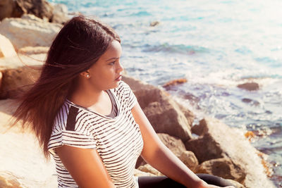 Young woman looking away while standing on rock at beach