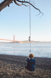 Rear view of woman sitting on swing with golden gate bridge in background