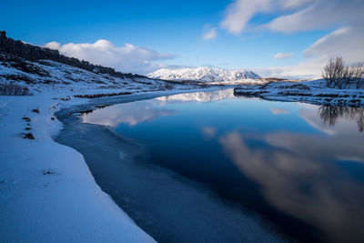 Frozen lake by mountain against sky during winter