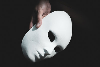 Cropped hand of person holding mask against black background