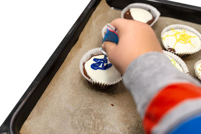 A child squeezes colored frosting from a tube onto chocolate brown cupcakes covered white frosting.