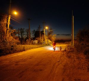 Man walking on illuminated road against sky at night