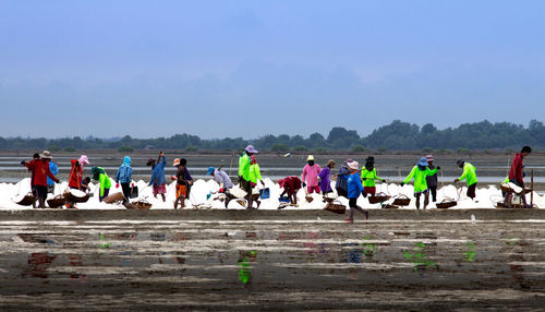 Group of fishermen working at beach against sky