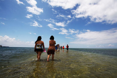 Rear view of people at beach against sky