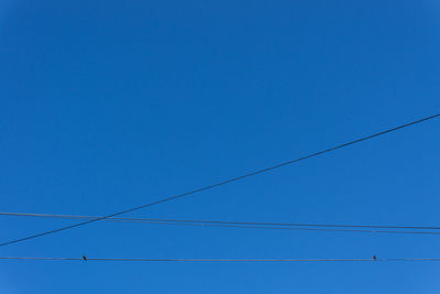 Low angle view of power lines against clear blue sky