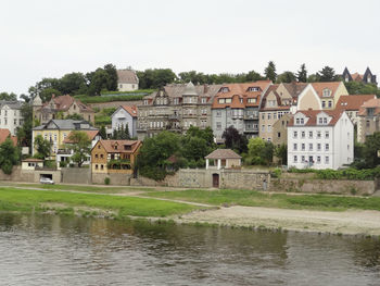Houses by river and buildings against sky