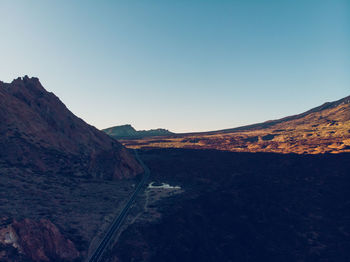 Road leading towards mountains against clear blue sky