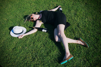 High angle view of young woman with champagne bottles lying on grassy field