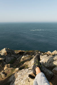 Low section of person on rock by sea against clear sky