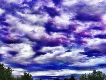 Low angle view of trees against cloudy sky