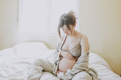 Pregnant woman sitting on bed at home