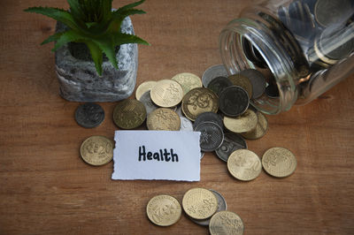 Health text on torn paper with jar, coins, and plant background. health and savings concept