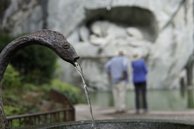 Close-up of water fountain with old married couple in background