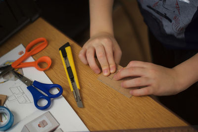 Cropped image of child hand with work tools and paper at table