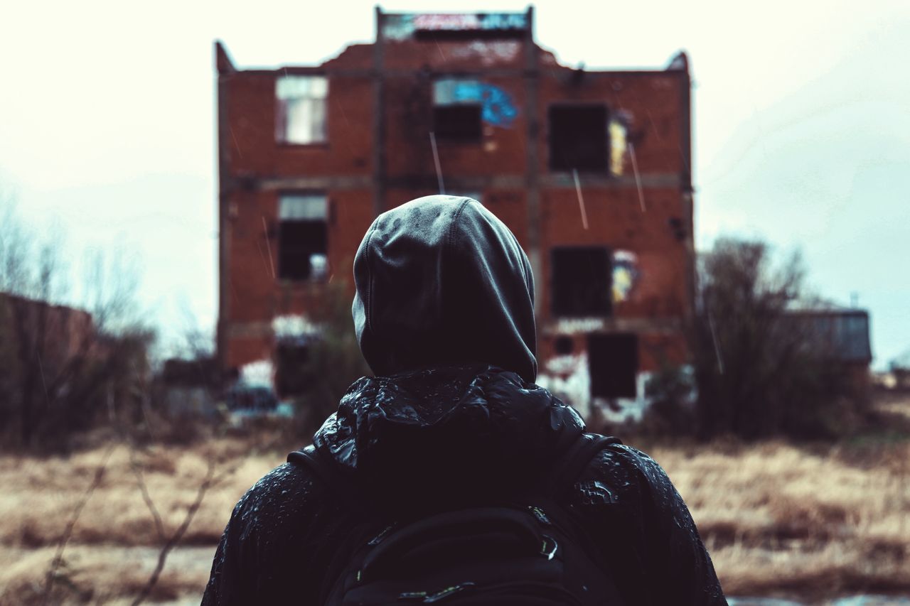 lifestyles, rear view, building exterior, casual clothing, leisure activity, focus on foreground, men, built structure, standing, waist up, architecture, warm clothing, three quarter length, hooded shirt, house, person, field, outdoors