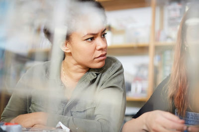 Mid adult technician looking away while sitting by female colleague at workshop