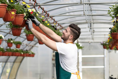 Side view of young man standing by potted plants