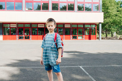 Portrait of a schoolboy with a backpack on his back standing against the backdrop of the school. 