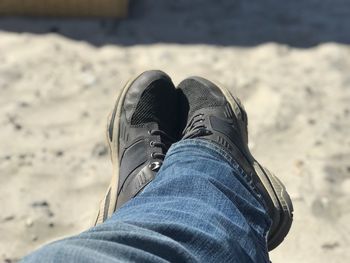 Low section of person wearing shoes on sand