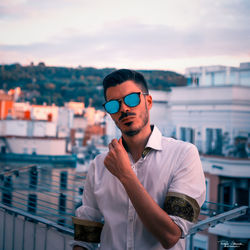 Young man standing against cityscape at sunset