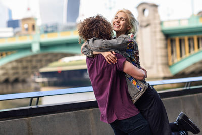 Happy friends standing on bridge in city