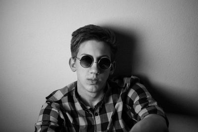 Portrait of young man wearing sunglasses against wall