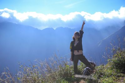 Portrait of happy excited woman showing peace sign on peak against mountains