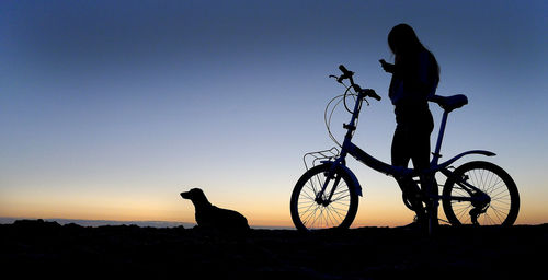 Silhouette man with bicycle against clear sky during sunset