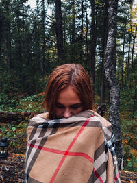 Woman wrapped in scarf standing against trees in forest