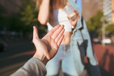 Cropped hand gesturing towards woman standing on footpath in city during sunny day