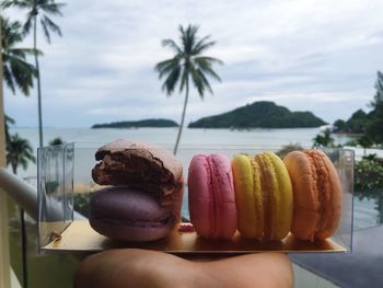 Cropped image of hand holding container with macaroons against sea