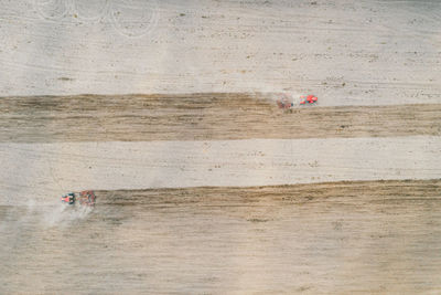 Red tractors plowing farm field aerial view looking down.