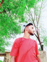 Young man looking away while standing against tree