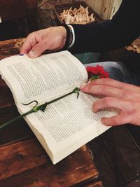 High angle view of woman reading book with red flower on table