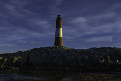 Low angle view of lighthouse on rock by building against sky
