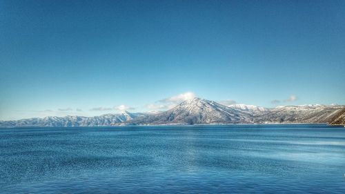 Scenic view of lake by snowcapped mountains against clear blue sky