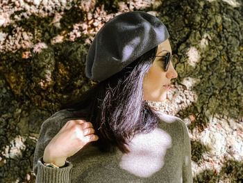 Young adult candid woman in casual sweater and grey french beret by old tree. autumnal spring outfit