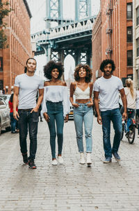 Full length of friends walking on street with manhattan bridge in background 