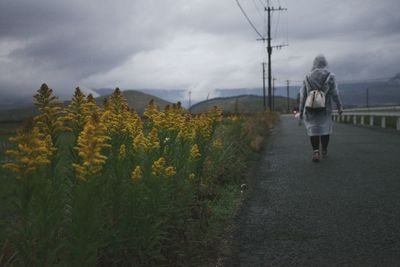 Rear view of woman walking on field against sky