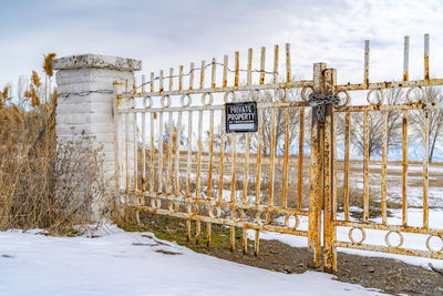 Fence on snow covered field against sky