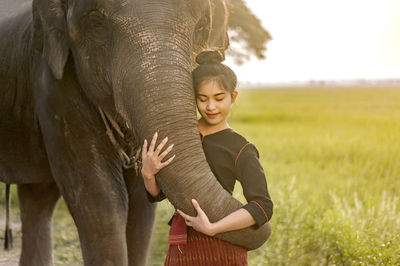 Smiling woman standing with elephant on field against sky