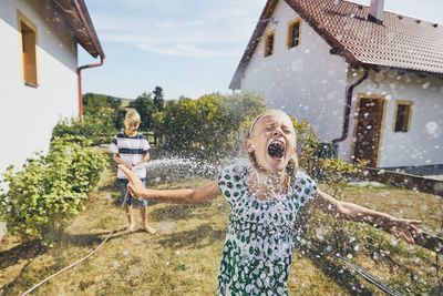 Boy spraying water on sister standing in yard