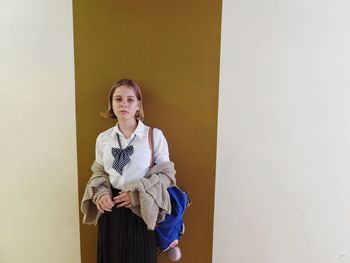 Portrait of young woman standing against wall