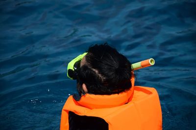 Rear view of man wearing life jacket and scuba mask while swimming in sea